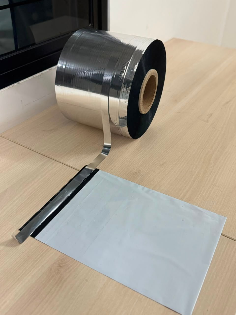 Roll of silicone-coated metallised release film unwinding onto a white poly mailer