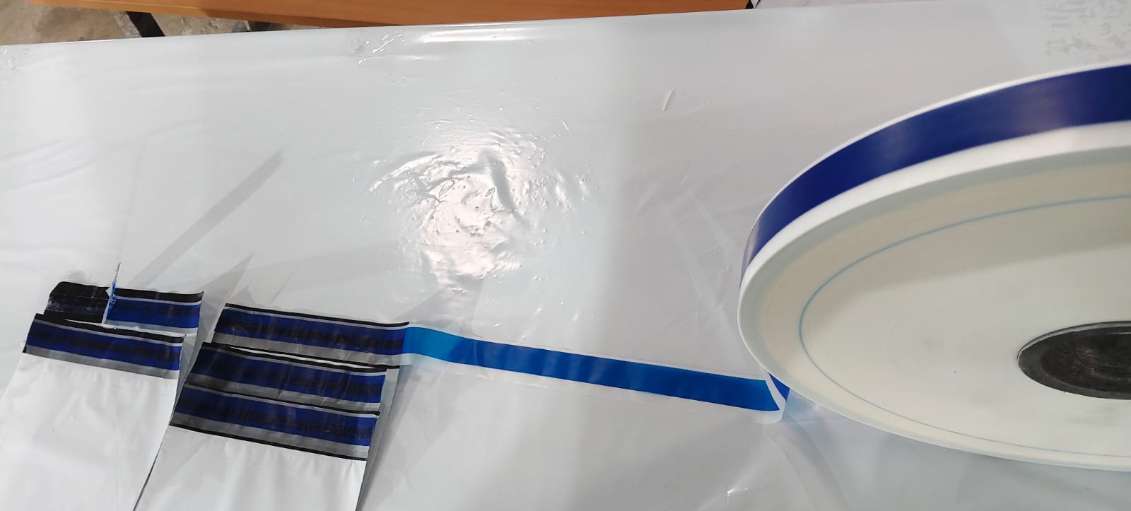 Blue tamper-evident release film on a reel beside white bags sealed with the blue security closure