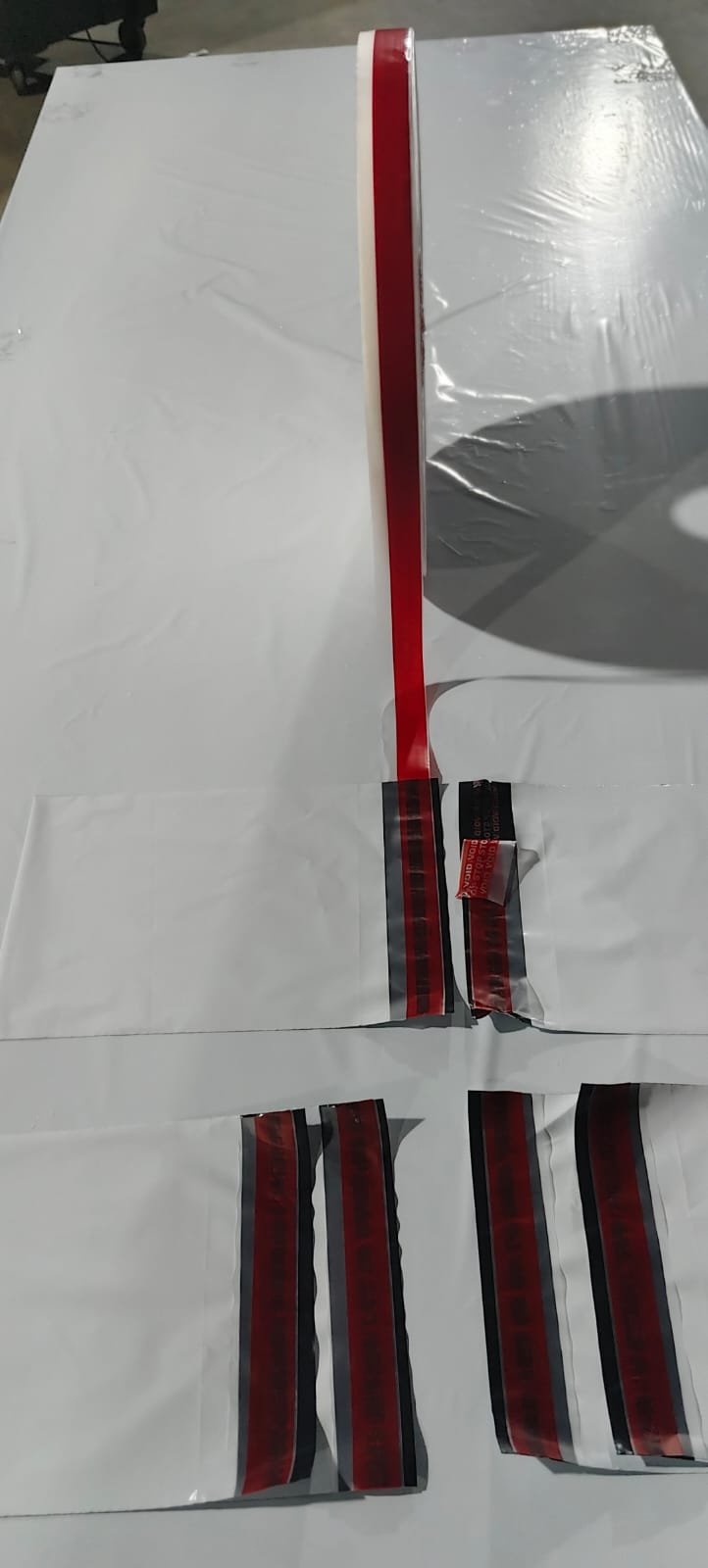 Several poly mailers sealed with red tamper-evident film, one lifted to show the VOID message transferred beneath
