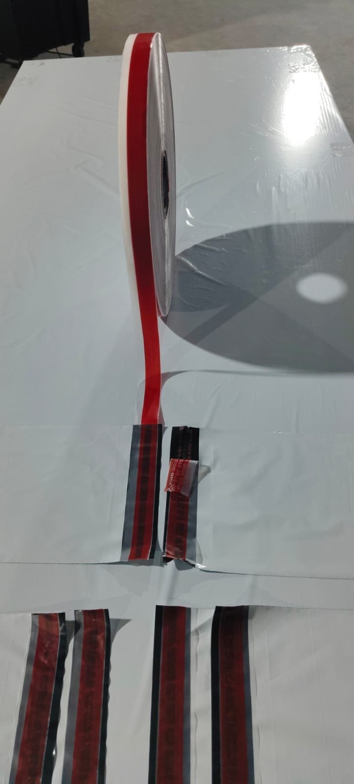 Red tamper-evident release film unwinding from its roll onto white poly bags, with VOID evidence showing on an opened seal